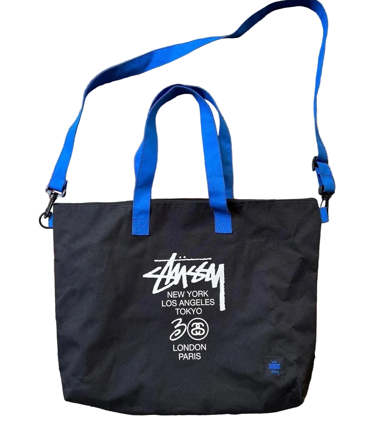 Black tote bag with blue straps and Stussy branding on a patterned rug